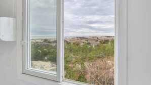 Ein Zimmer mit einem großen Fenster, das Blick auf eine Küstenlandschaft mit Hügeln und spärlicher Vegetation bietet.