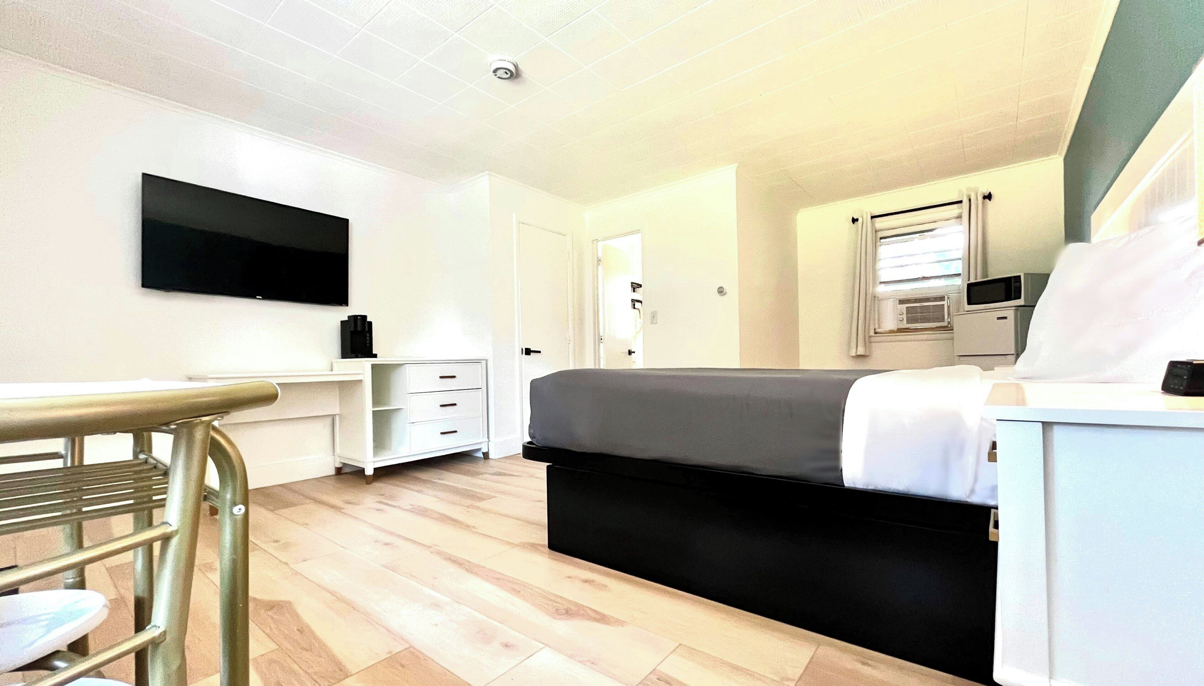 A hotel room with a bed, a desk with a chair, a television, a wardrobe, and a window with curtains.