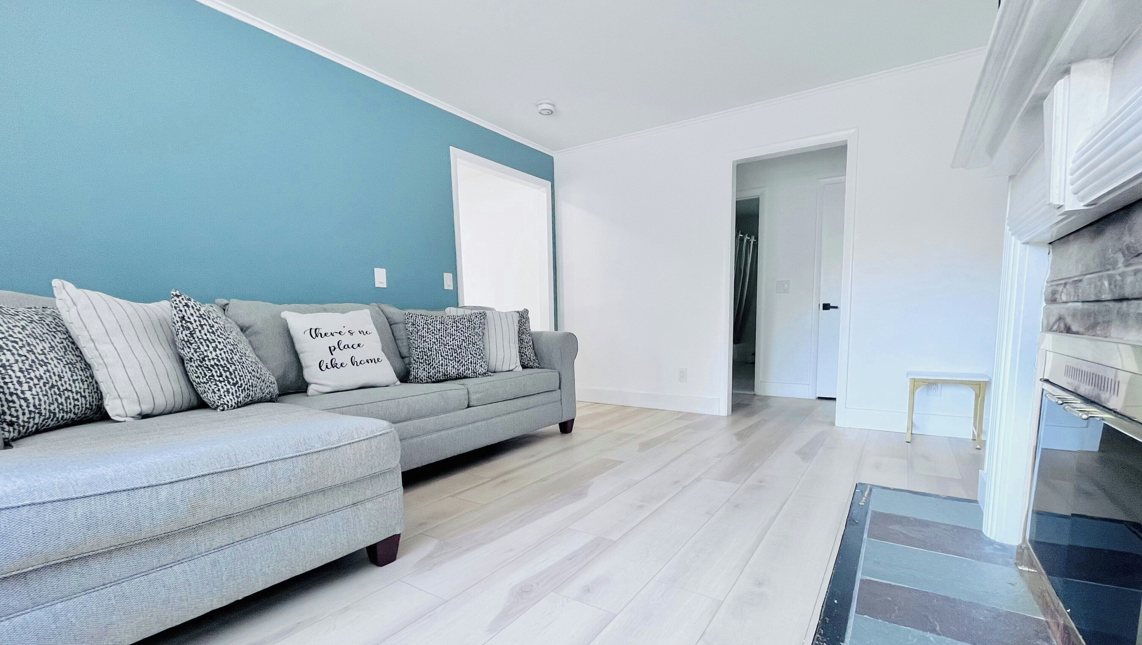 Un salon moderne avec un canapé gris, des coussins à motifs et un mur d’accent bleu.