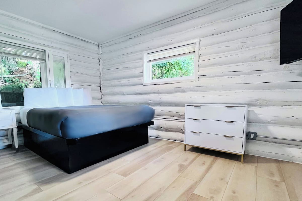 A bedroom with a bed, a desk, a dresser, and a window.