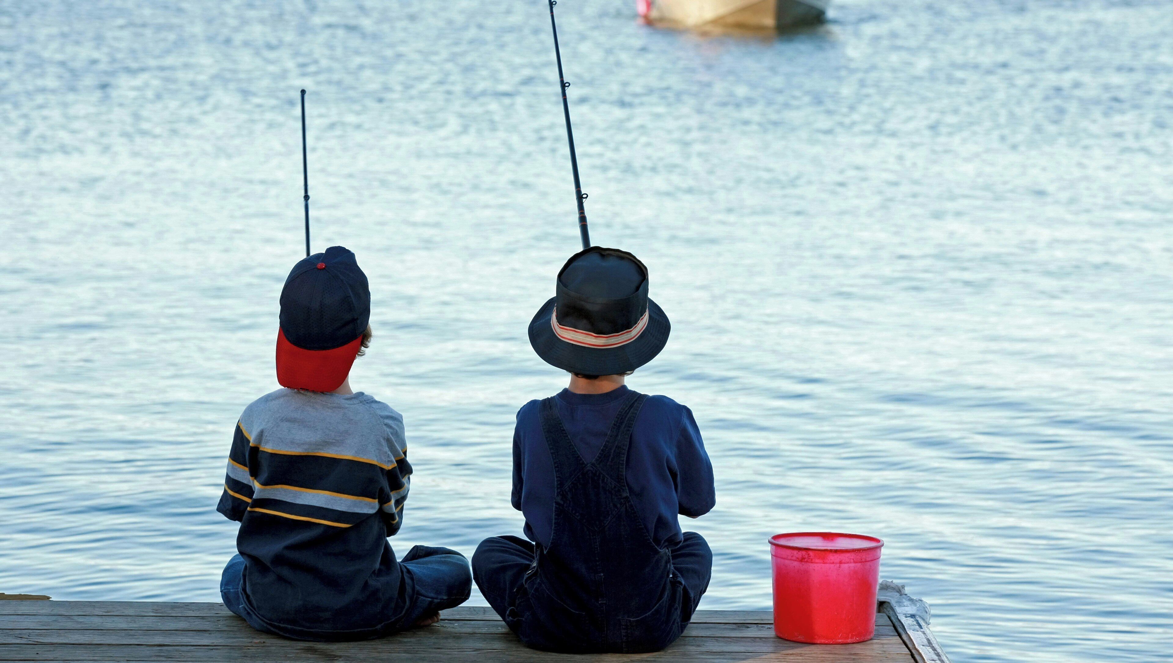 Two individuals sitting on a wooden dock by a calm body of water, fishing.