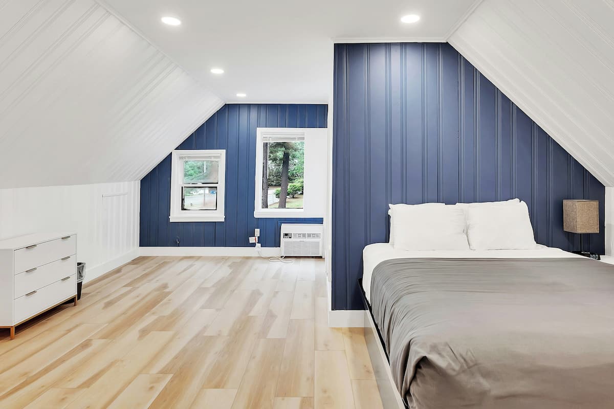 A bedroom with a sloped ceiling, a bed, a dresser, a window, and a radiator.