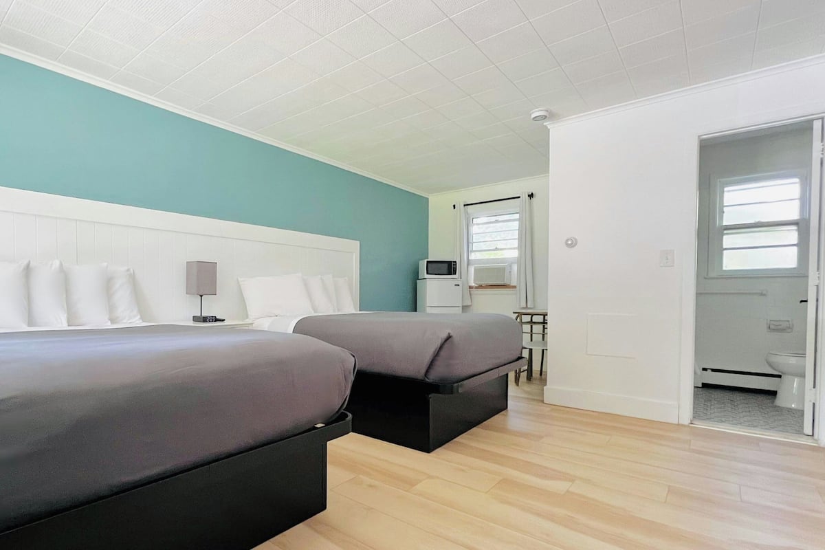 A hotel room with two beds, a desk, a chair, a microwave, and a bathroom visible through an open door.