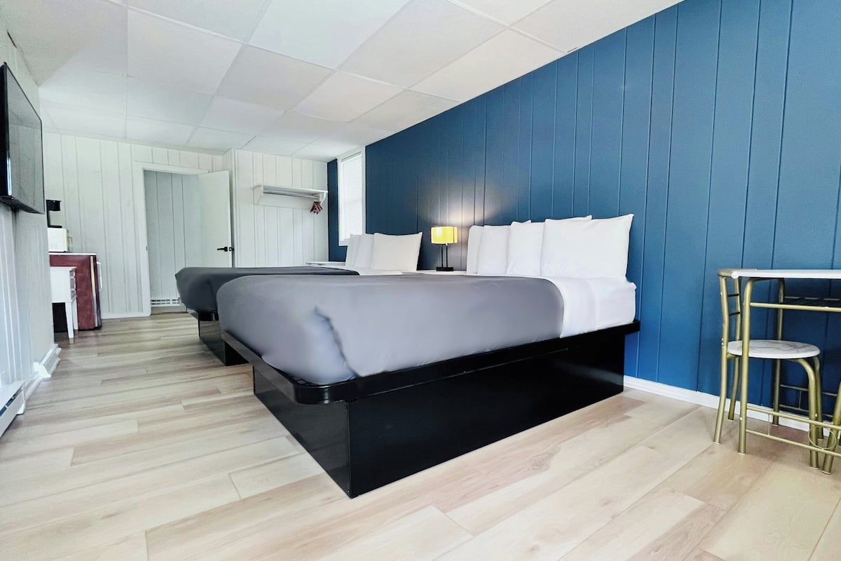 A hotel room with a bed, bedside table, lamp, and a small table with stools.
