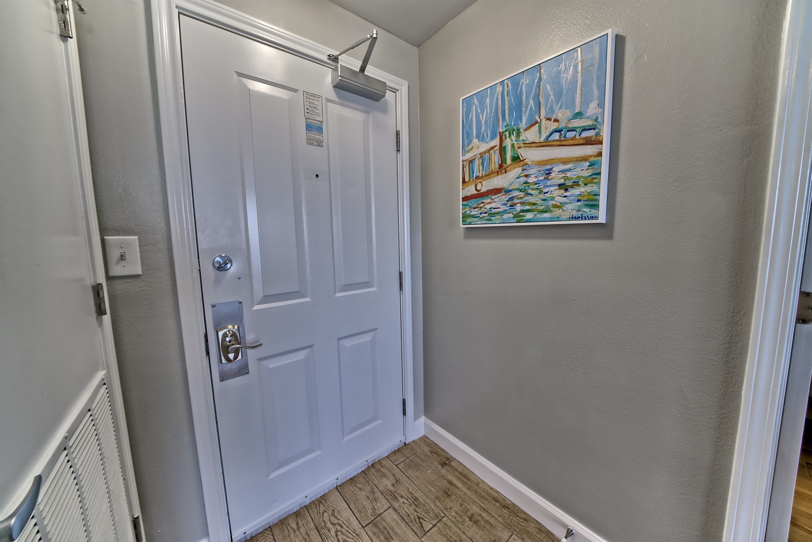 A hallway with a white door, a painting of a sailboat on the wall, and a vent on the left.