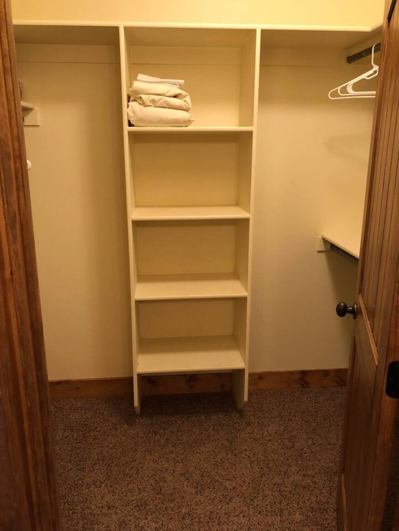A closet with three shelves and a hanging rod, containing folded clothes and a hanging garment.