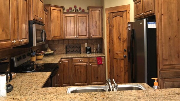 A kitchen with wooden cabinets, granite countertops, a stainless steel sink, a microwave, a stove, and a refrigerator. - Second Level Condo - BJ#6 (Driggs)