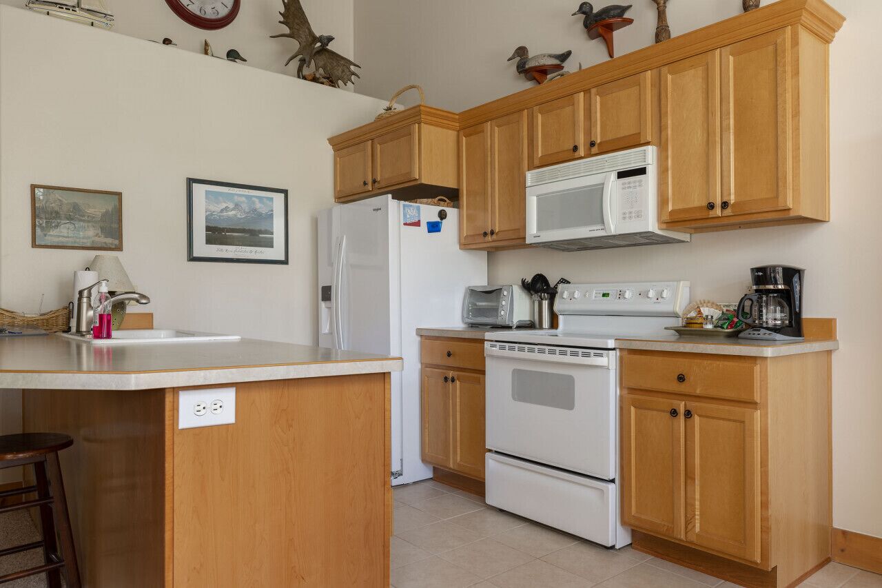 A kitchen with wooden cabinets, a white refrigerator, a microwave, a stove, and a coffee maker.