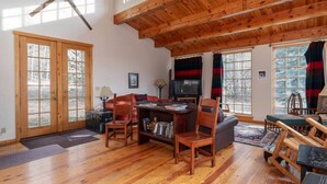 A spacious living room with wooden floors, a high ceiling, and large windows. - Windigo Lodge with Hot Tub (Victor)