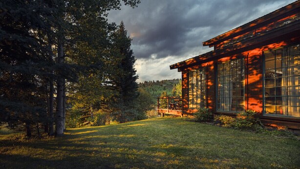 A rustic cabin with large windows, surrounded by a grassy yard and dense trees. - Windigo Lodge with Hot Tub (Victor)