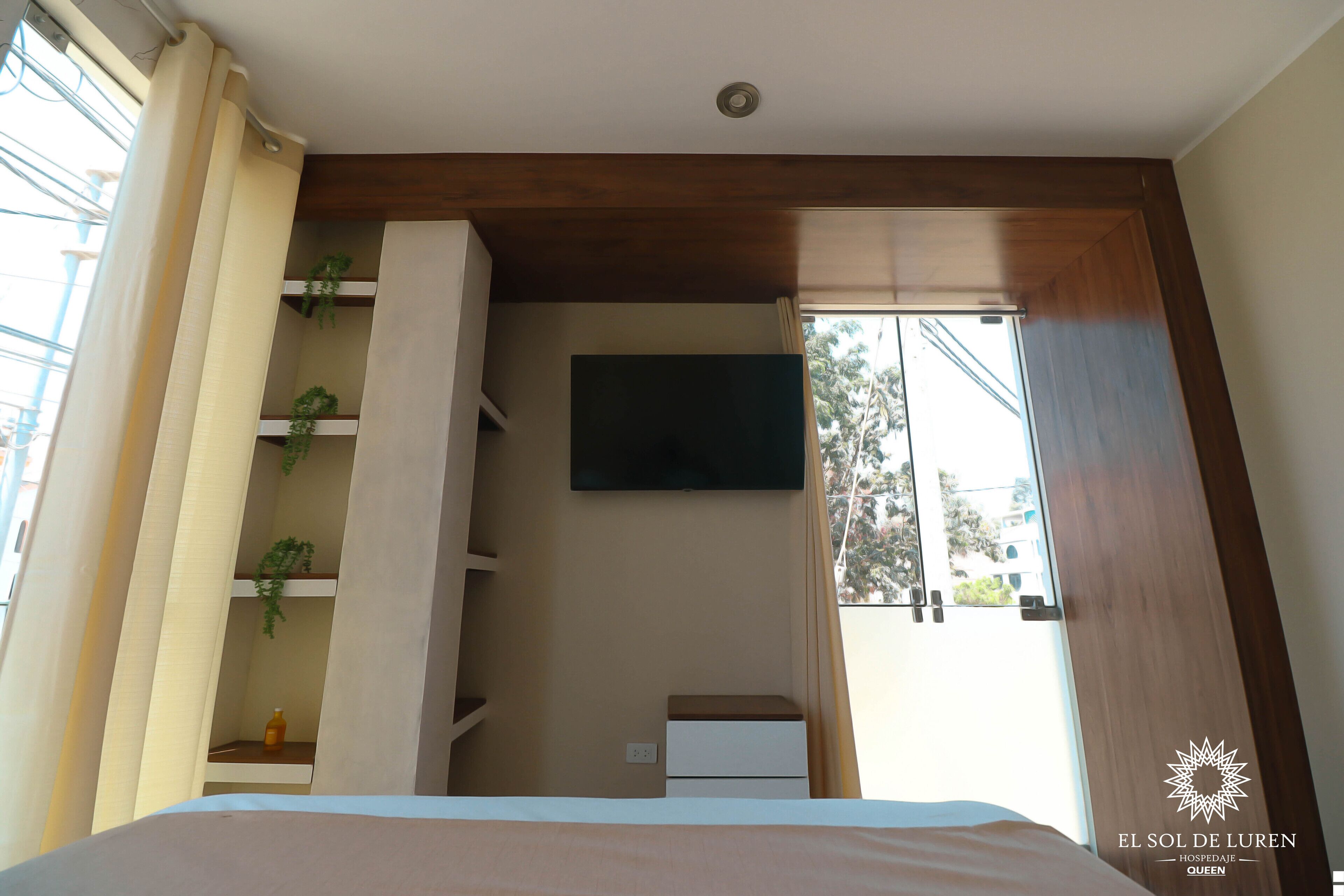 Una camera da letto con un letto, una TV a muro e una finestra con tende.