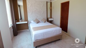 A hotel room with a bed, a bedside table, a mirror, and a door. - SOL DE LUREN PUENTE BLANCO (Ica)