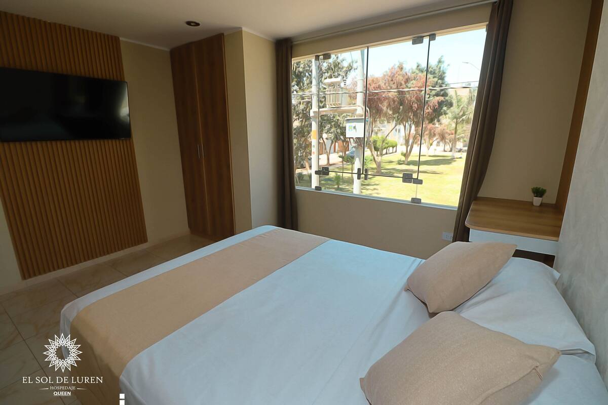Une chambre d’hôtel avec un grand lit, un téléviseur fixé au mur et une fenêtre donnant sur l’extérieur.