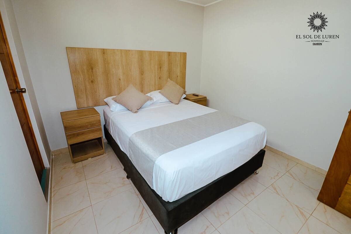 Une chambre à coucher bien aménagée, avec une tête de lit en bois, un lit recouvert de draps blancs, une table de chevet et une commode en bois.