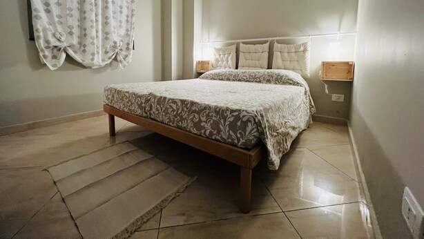 A bedroom with a bed, a nightstand, a lamp, and a window with curtains. - Sweet Home - 101 (Catania)