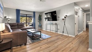 A modern living room with a sofa, coffee table, and a flat-screen TV mounted on the wall. - 2 bed/ 2 bath condo * Balcony * King Bed (Pensacola)