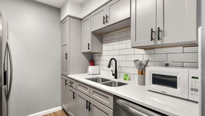 A modern kitchen with grey cabinets, a stainless steel refrigerator, a coffee maker, and a microwave. - 2 bed/ 2 bath condo * Balcony * King Bed (Pensacola)