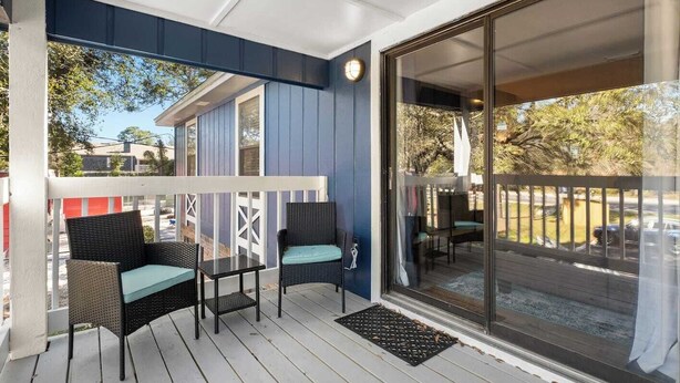A covered outdoor area with two wicker chairs and a small table, a sliding glass door leading to a deck, and a blue exterior wall. - 2 bed/ 2 bath condo * Balcony * King Bed (Pensacola)