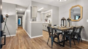 A modern dining area with a wooden table and chairs, a large mirror, and a kitchen in the background. - 2 bed/ 2 bath condo * Balcony * King Bed (Pensacola)