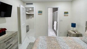 Ein Schlafzimmer mit Bett, Fernseher, Kleiderschrank, Badezimmer mit Dusche und Nachttisch mit Lampe.