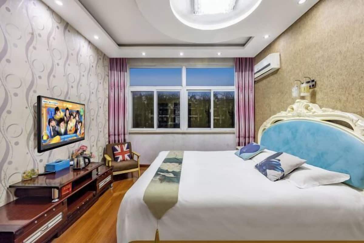 Habitació d'hotel amb llit, televisió, escriptori i finestra amb cortines.