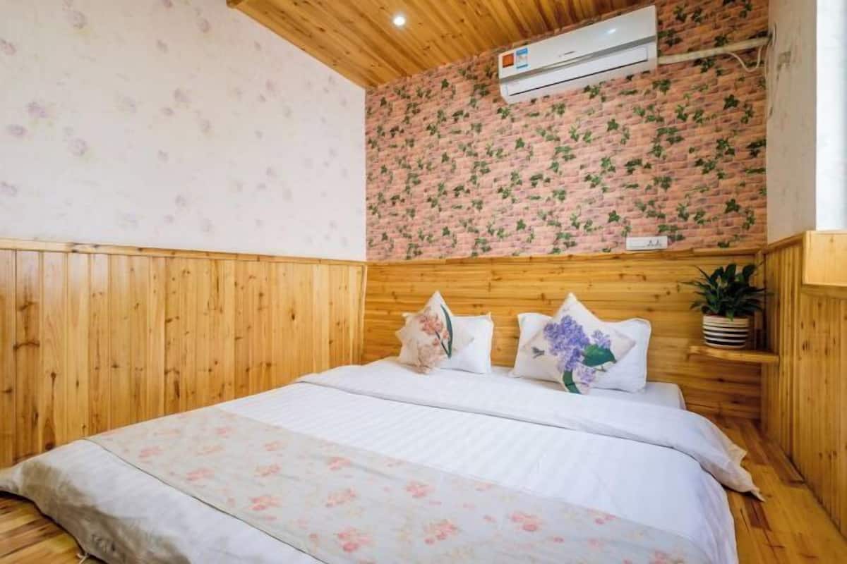 Habitació amb sostre de fusta, paret de maó i llit amb roba de llit floral, a més d'una planta en test.