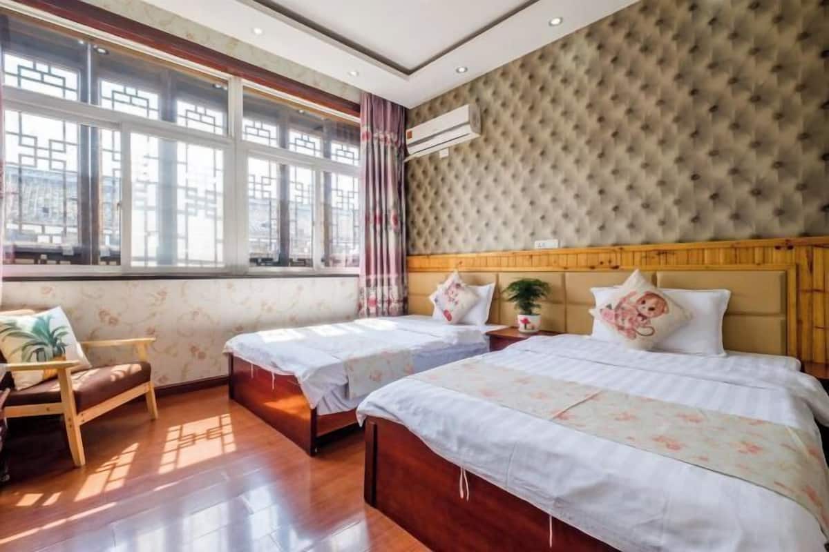Habitació d'hotel amb dos llits, una cadira de fusta, una finestra amb cortines i un aire condicionat fixat a la paret.