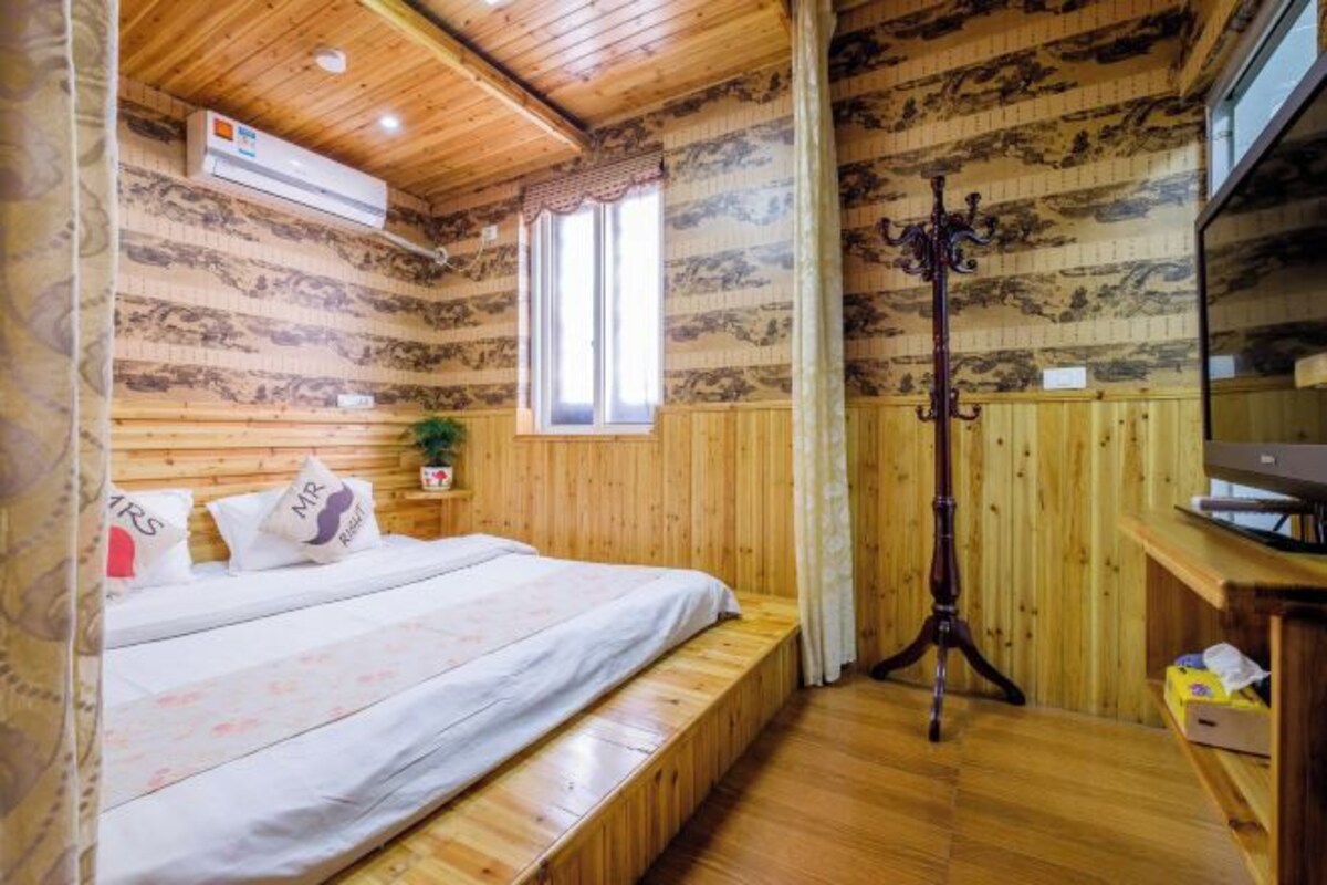Una habitación con paneles de madera, una cama, un ventanal, una lámpara de pie y un televisor.