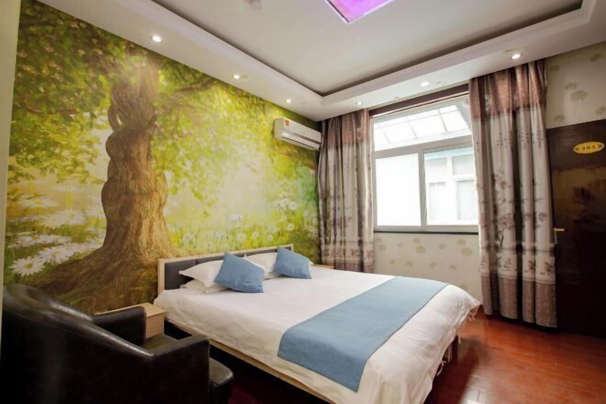 Un dormitorio con cama, mesita de noche, una silla, ventana con cortinas y un mural en la pared.