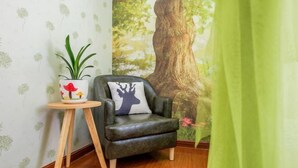 A cozy room with a dark leather armchair, a small wooden side table with a potted plant, and a large tree mural on the wall.
