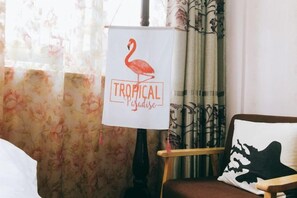 A room with a bed, a chair with a pillow, a whiteboard with a flamingo and the words 'Tropical Paradise,' and a window with curtains. - Wuzhen Xizha Country Cottage Homestay (Tongxiang)