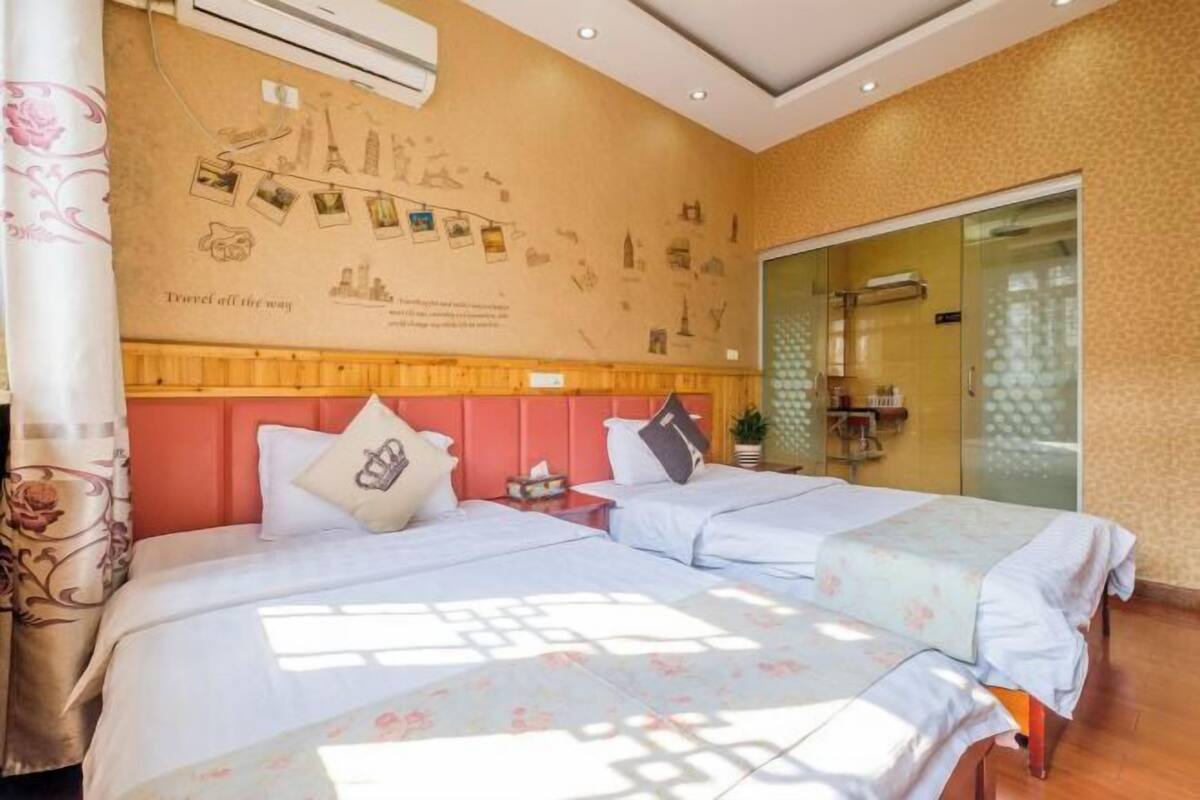 Habitació d'hotel amb dos llits, un panell de fusta al capçal, una cabina de dutxa de vidre i una paret decorada amb fotografies de viatges.