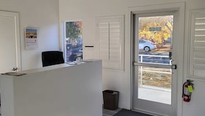 A reception area with a desk, a bulletin board, a door with an exit sign, and a view of a parking lot with autumn trees. - Stafford Inn (Redwood City)