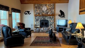 A spacious living room with a stone fireplace, wooden ceiling, and black leather furniture. - Beautiful Fall Foliage & Excellent Fishing on the Crown Jewel in the Northwoods (Mercer)