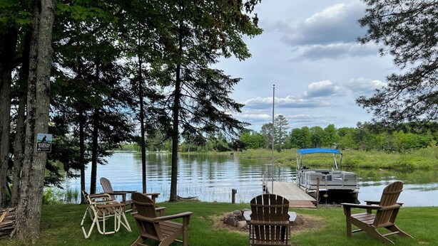 A lakeside deck with Adirondack chairs, a dock with a boat, and a wildlife sign. - Beautiful Fall Foliage & Excellent Fishing on the Crown Jewel in the Northwoods (Mercer)