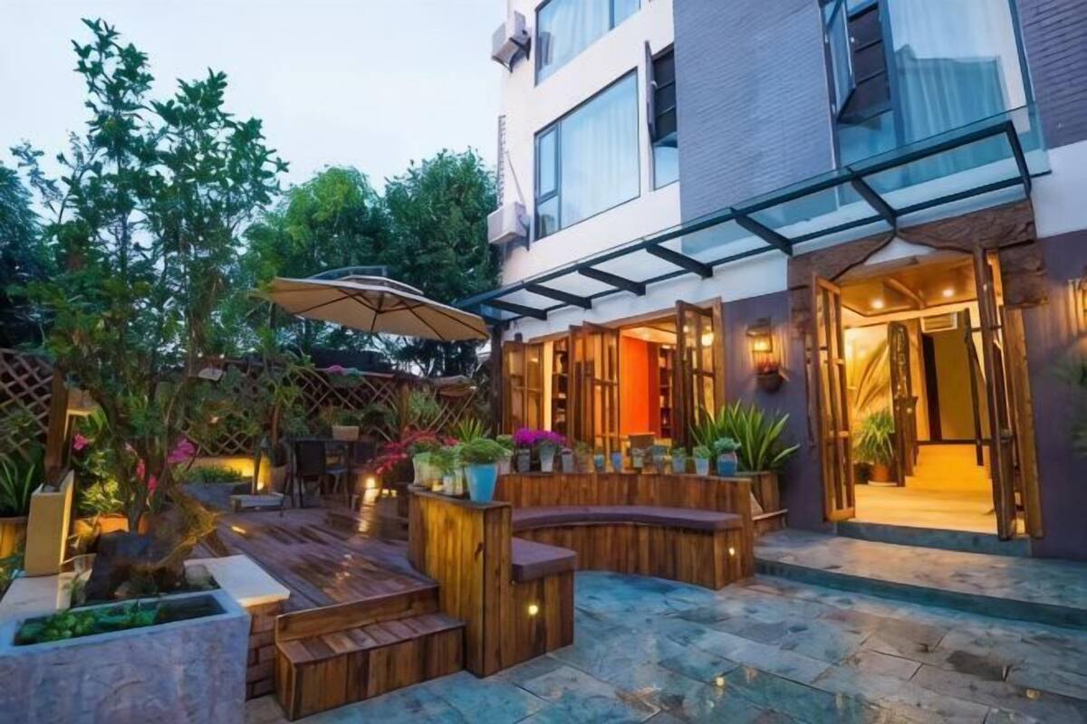 A courtyard with wooden seating, potted plants, and a glass-enclosed entrance to a building.