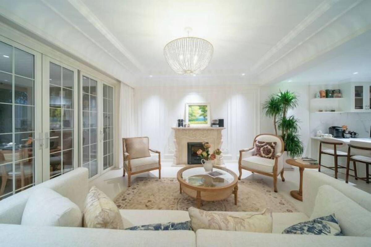 A spacious living room with a fireplace, comfortable seating, and a view of the kitchen.