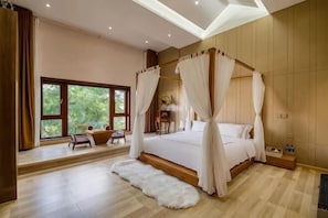 A bedroom with a four-poster bed, a large window, a small table, and a white fur rug.