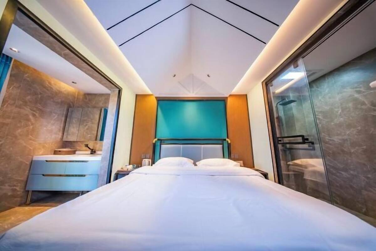 A modern hotel room with a large bed, a vanity with a mirror, and a shower area.