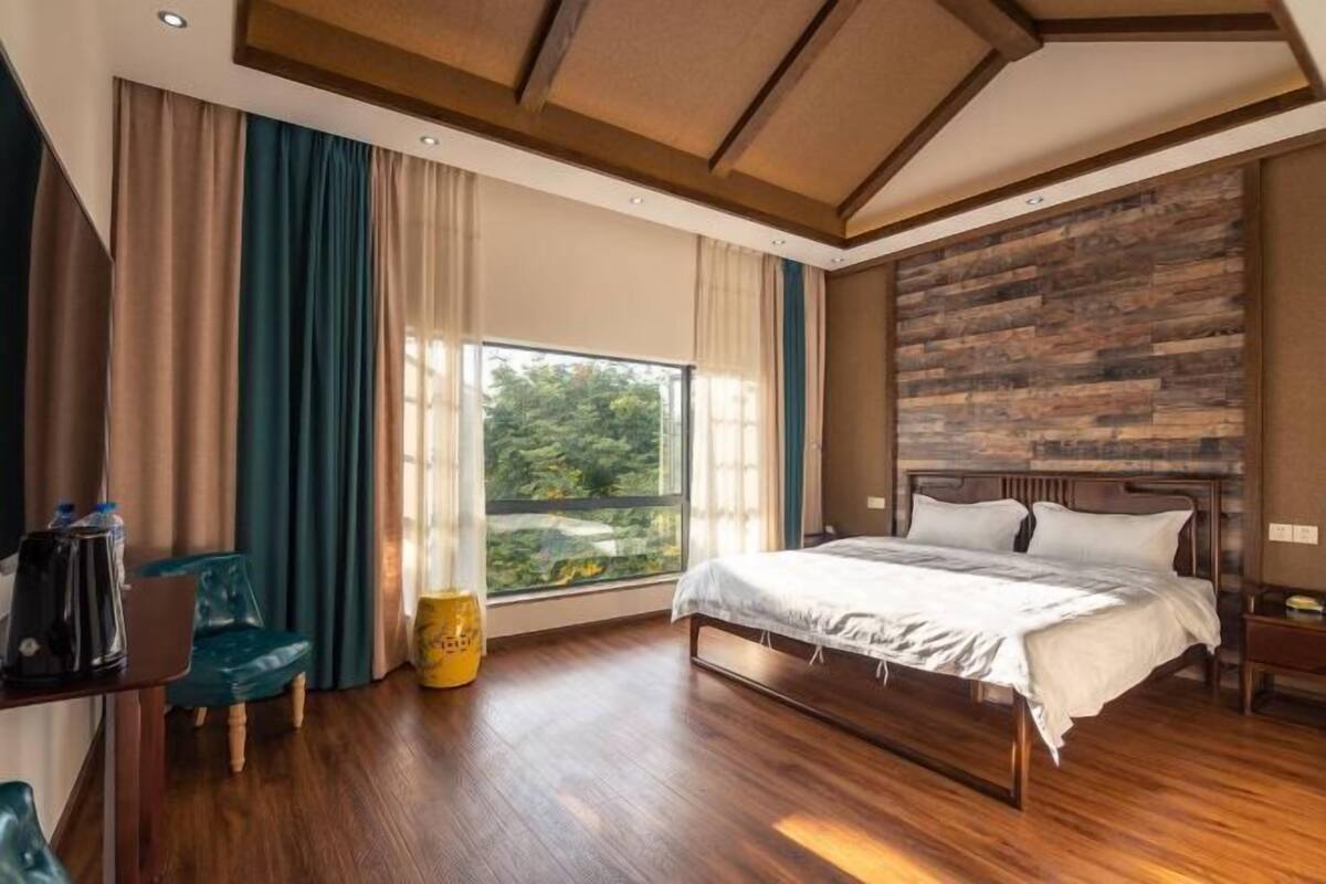 A bedroom with a large window, wooden flooring, a bed with white bedding, and a wooden headboard.