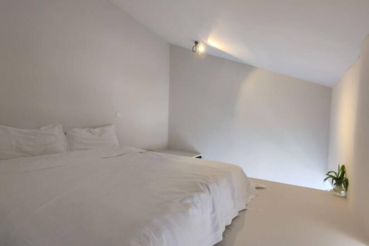 A minimalist bedroom with a bed, a small bedside table, and a wall-mounted light fixture.