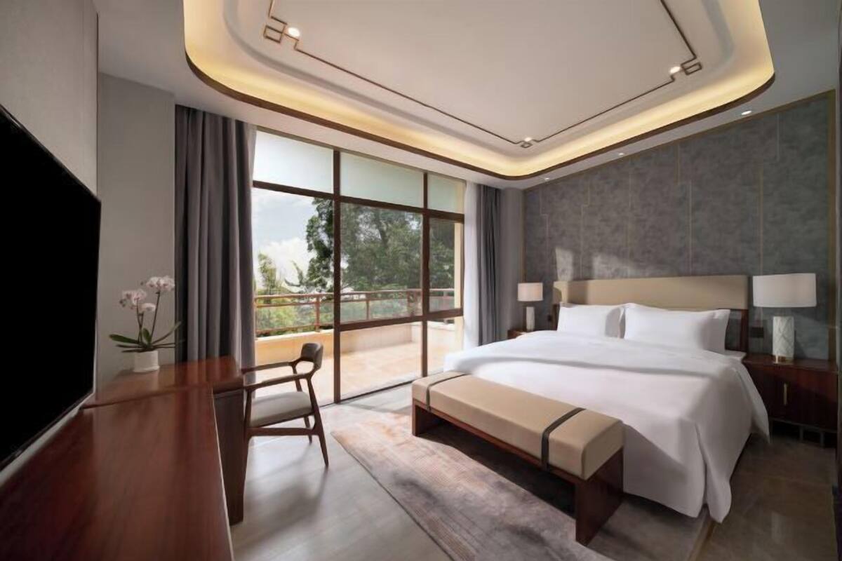 A modern hotel room with a large bed, a TV, a desk, and a balcony with a view.