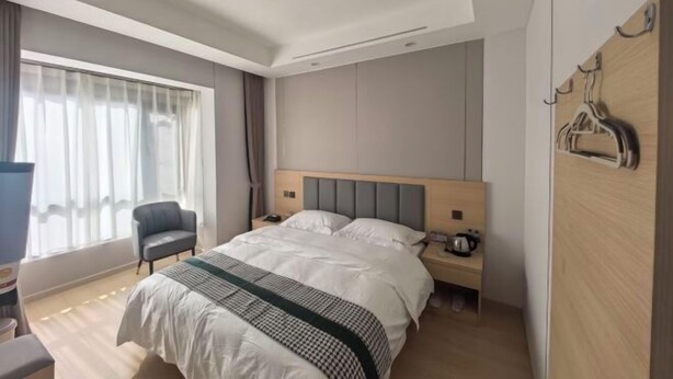 Une chambre d’hôtel moderne avec un grand lit, une table de chevet avec une lampe, une chaise et une armoire avec des patères.