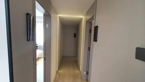 Un couloir étroit au plancher de bois, qui mène à une chambre à coucher équipée d’un lit et d’une table de chevet.