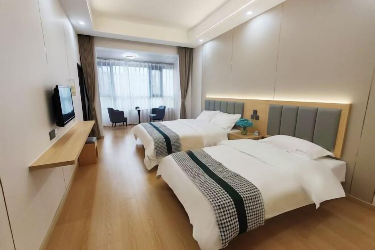 Habitación de hotel con dos camas, televisión, escritorio y vistas al exterior.