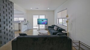En moderne stue med en mørk sofa, et sofabord og et fladskærms-tv i baggrunden.
