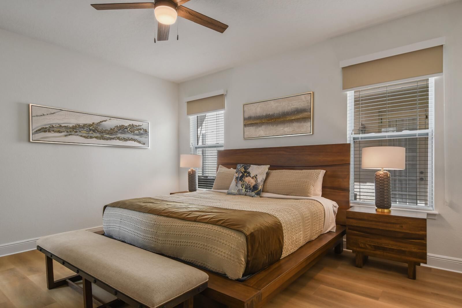 A bedroom with a bed, bench, bedside tables, and ceiling fan.