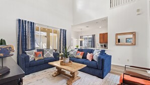 Een ruime woonkamer met een blauwe bank, een houten bijzettafeltje en een groot raam met gordijnen.