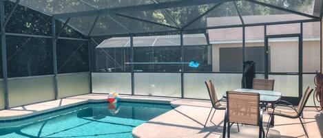 Piscina cubierta al aire libre con sillas de descanso y una mesa, rodeada por una valla de metal.