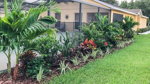 A modern building with a glass enclosure, surrounded by a well-maintained garden with various plants and flowers. - South Facing Pool at Sandy Ridge! (Davenport)